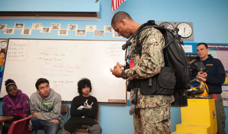 Navy diver wearing G-Shock Frogman GW200 while demonstrating scuba gear to students.